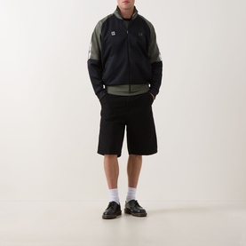 Model wearing Fred Perry Meyba Taped Track Jacket in Black with khaki panels, paired with black shorts and white socks.