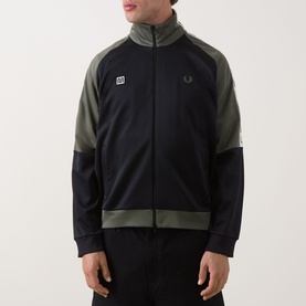 Model wearing Fred Perry Meyba Taped Track Jacket in Black, two-tone with khaki panels, zip-through, laurel wreath logo, paired with dark trousers