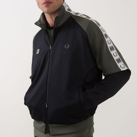 Model wearing Fred Perry Meyba Taped Track Jacket in Black, with contrast khaki sleeves, logo taping, high neck and two-way zip