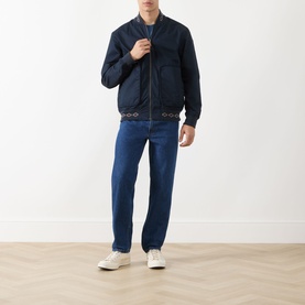 Model wearing Scotch & Soda Reversible Printed Bomber Jacket in Sky Captain with blue jeans and white trainers