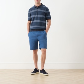 Model wearing Scotch & Soda Ensign Blue chino shorts, styled with a navy striped polo shirt and dark canvas trainers.