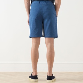 Model wearing Scotch & Soda Ensign Blue chino shorts, rear view, styled with navy slip-on shoes