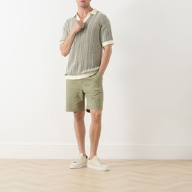 Model wearing Scotch & Soda Oil Green 300 chino shorts, styled with a sage knit polo shirt and white trainers