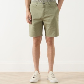 Model wearing Scotch & Soda Oil Green chino shorts in cotton-elastane blend, styled with white low-top trainers.