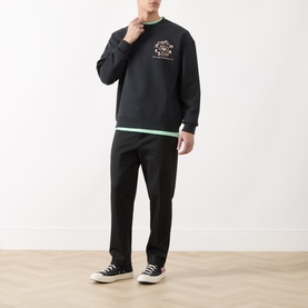 Model wearing Scotch & Soda Floral Graphic Logo Sweatshirt in Meteorite with black trousers and white high-top trainers.