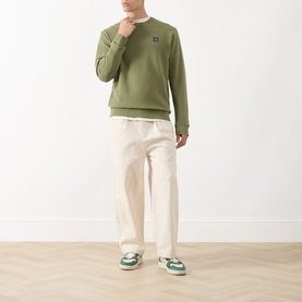 Model wearing Scotch & Soda Seasonal Essentials Logo Badge Sweatshirt in Oil Green 300, styled with cream wide-leg trousers and green trainers