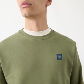 Model wearing Scotch & Soda Seasonal Essentials Logo Badge Sweatshirt in Oil Green, crew neck, with blue logo badge on chest. Styled with white