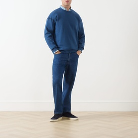 Model wearing Scotch & Soda Ensign Blue crew neck sweatshirt with mid-blue straight-leg jeans and navy trainers.