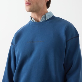 Model wearing Scotch & Soda Ensign Blue crew neck sweatshirt in 100% cotton, styled over a chambray shirt