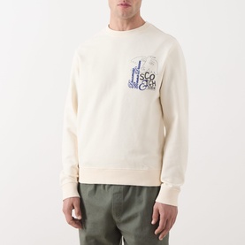Model wearing Scotch & Soda Work-Out Art Logo Sweatshirt in Eggnog, crew neck with blue chest logo graphic, paired with olive shorts.