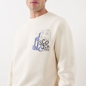 Model wearing Scotch & Soda Work-Out Art Logo Sweatshirt in Eggnog, crew neck with blue graphic logo print to chest.