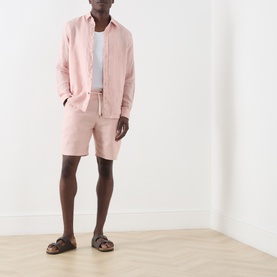 Model wearing Scotch & Soda Fave Bermuda Shorts in Misty Rose, styled with matching linen shirt, white tee, and brown sandals.