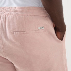 Model wearing Scotch & Soda Fave Bermuda Shorts in Misty Rose, showing rear welt pocket and logo patch detail.