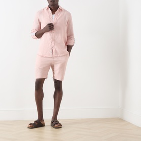 Model wearing Scotch & Soda Fave Bermuda Shorts in Misty Rose, paired with matching pink linen shirt and brown sandals.