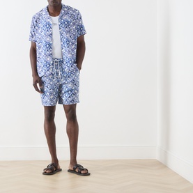 Model wearing Scotch & Soda Tile Flower Printed Bermuda Shorts in blue tile print, styled with matching printed shirt and black sandals.