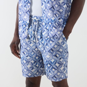 Model wearing Scotch & Soda Tile Flower Printed Bermuda Shorts in blue geometric print with elasticated drawstring waist, styled with matching shirt.