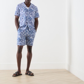 Model wearing Scotch & Soda Tile Flower Printed Bermuda Shorts in blue floral tile print, styled with matching shirt and brown sandals.