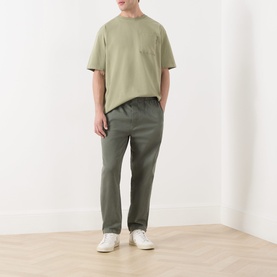 Model wearing Scotch & Soda 3 Crosses Logo T-Shirt in Oil Green 300, round neck, short sleeves, styled with khaki trousers and white trainers.