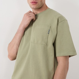 Model wearing Scotch & Soda 3 Crosses Logo T-Shirt in Oil Green 300, with chest pocket and XXX logo detail, round neck, short sleeves.