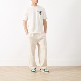 Model wearing Scotch & Soda Artwork Logo T-Shirt in Eggnog, with cream wide-leg trousers and green trainers