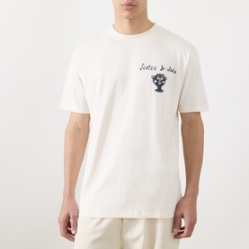 Model wearing Scotch & Soda Artwork Logo T-Shirt in Eggnog, crew neck, short sleeves, small chest logo graphic, styled with cream trousers.