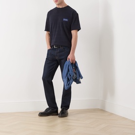 Model wearing Scotch & Soda Logo Texture Jacquard Stripe T-Shirt in Sky Captain with dark indigo jeans and black shoes, carrying a denim jacket.