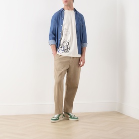 Model wearing Scotch & Soda Work-Out Art Logo T-Shirt in Eggnog with blue overshirt, tan trousers and green trainers.