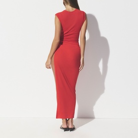 Model wearing Skims Carmine red sleeveless maxi dress, shown from behind, with ruched side detail and form-fitting silhouette
