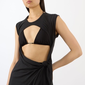 Model wearing Skims Sarong Dress in Onyx, featuring a cut-out chest detail and knotted wrap skirt in sleeveless black stretch fabric.