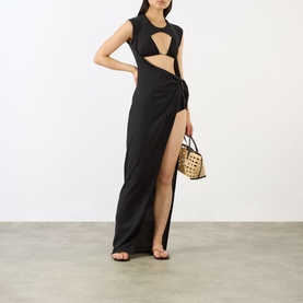 Model wearing Skims Sarong Dress in Onyx, black cut-out maxi with twist front and high slit, styled with woven basket bag and strappy sandals.
