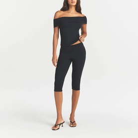 Model wearing Skims Obsidian cropped leggings with matching off-shoulder top and strappy heeled sandals