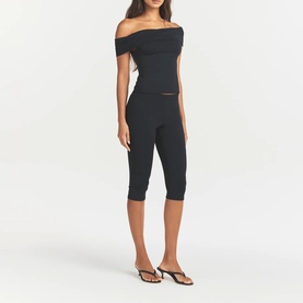 Model wearing Skims Obsidian cropped leggings with matching off-shoulder top and black strappy flat sandals.