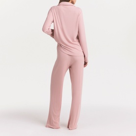 Model wearing Skims Pyjamas in Morganite, rear view, showing long-sleeve top with collar and wide-leg trousers in matching soft pink tone.