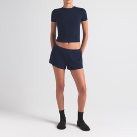 Model wearing Skims navy shorts with matching navy crop T-shirt, black ankle socks and black shoes.