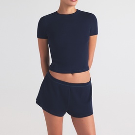 Model wearing Skims navy shorts styled with a matching navy cropped short-sleeve top