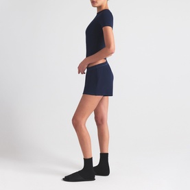 Model wearing Skims navy shorts with matching navy T-shirt and black ankle socks, side profile view