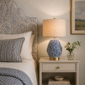 Mindy Browne Olivia Floral Table Lamp in blue ceramic with brass base and linen shade, styled on a bedside table in a bedroom setting.