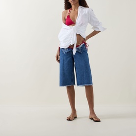 Model with Away That Day Gili Side-Tie Bikini Bottoms in Raspberry, styled with white knotted shirt and blue denim culottes