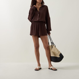 Model wearing Away That Day brown cover-up shirt and shorts set, styled with a woven tote bag and white flat sandals.
