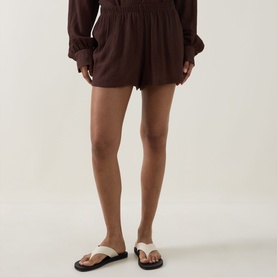 Model wearing Away That Day brown viscose-blend shorts with elasticated waist, styled with matching brown long-sleeve top and black slide sandals.