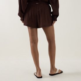 Model wearing Away That Day brown viscose shorts, shown from behind, styled with matching brown long-sleeve top and beige slides.