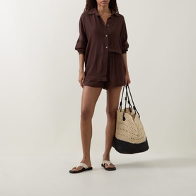 Model wearing Away That Day brown viscose shorts with matching shirt, styled with white sandals, carrying a straw tote bag.