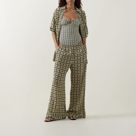 Model wearing Away That Day Navy/Gold Link Print swimsuit styled with matching wide-leg trousers and open shirt cover-up.