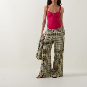 Model wearing Away That Day Raspberry swimsuit with wide-leg geometric print trousers and black flat sandals, carrying a matching scarf.