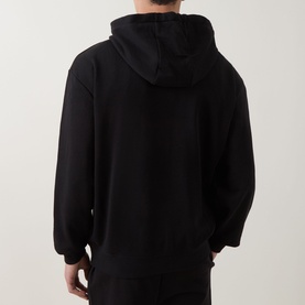 Model wearing Hugo black cotton hoodie, rear view showing hood and relaxed oversized fit with long sleeves.