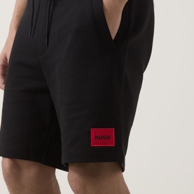 Model wearing Hugo black cotton shorts with red logo patch detail at hip