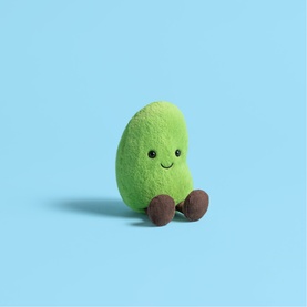 Jellycat green avocado soft toy with embroidered smile and small brown feet, seated against a light blue background