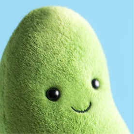 Jellycat green smiling avocado-shaped plush soft toy with beady eyes and velvety texture, shown against light blue background