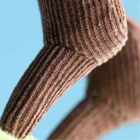 Jellycat plush toy close-up showing brown ribbed knit texture detail against a blue background, with a hint of green visible below.