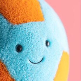 Jellycat plush soft toy ball with smiling face, in blue, orange and yellow fluffy fabric, close-up detail shot